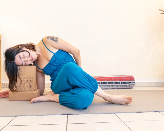 Young Ryu lying on her side with closed eyes, her head on a cork block, a bolster in the background – yin yoga at Studio Sonnenaufgang